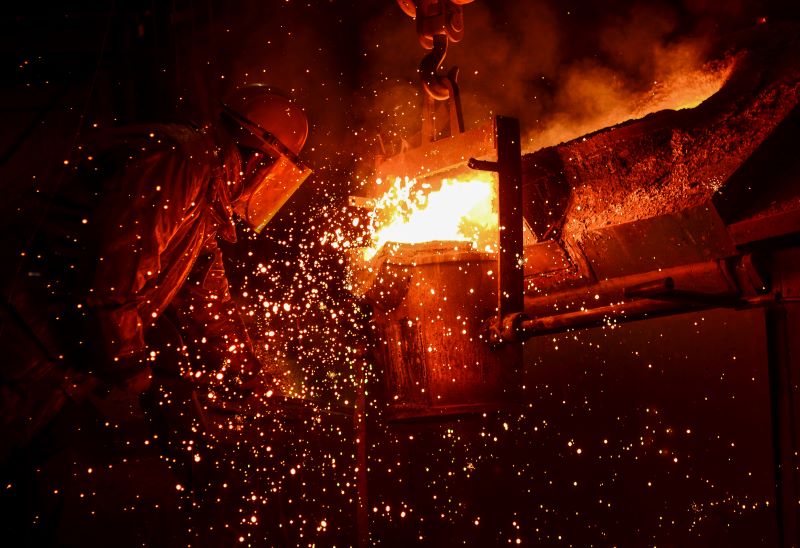 Ein Arbeiter im Schutzanzug bei der Metallschmelze mit glühenden Funken.