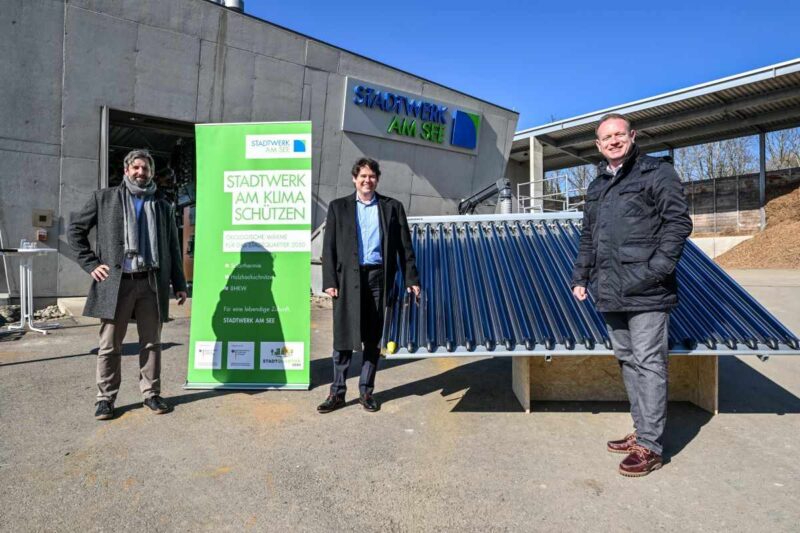 3 Personen freuen sich über einen Solarkollektor vor dem Eingang eines Betriebshofes der Stadtwerke am See