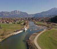 Blick auf einen Fluss mit neuem Wasserkraftwerk vor der Kulisse der Alpen.