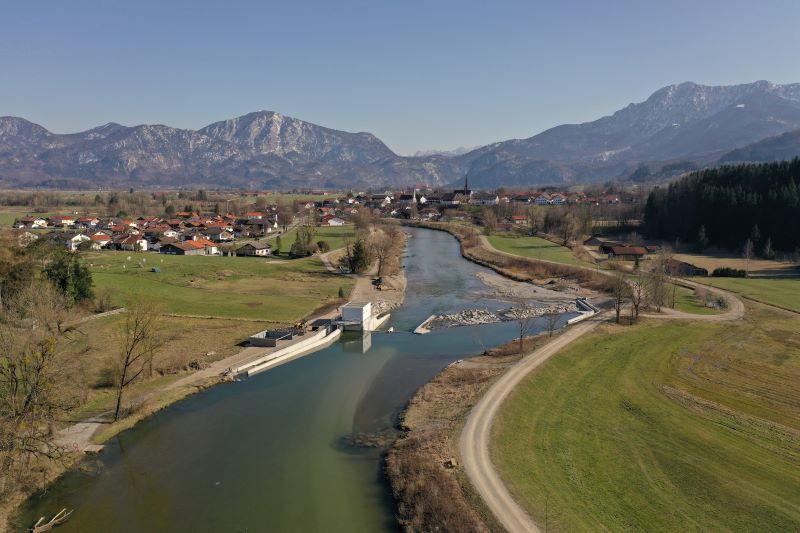 Blick auf einen Fluss mit neuem Wasserkraftwerk vor der Kulisse der Alpen.
