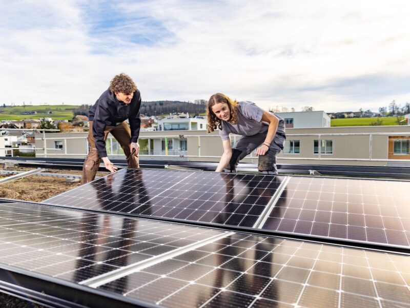 Ein junger Mann und eine junge Frau auf einem Dach halten ein Solar-Modul - die Schweiz führt neue Solarlehren ein.