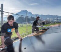 2 Installateure montieren Solarmodule - im Hintergrund schneebedeckte Berge.