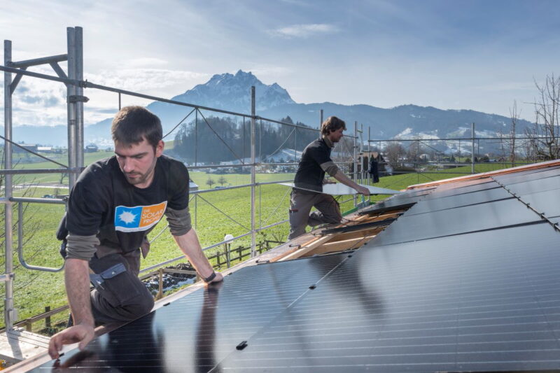 2 Installateure montieren Solarmodule - im Hintergrund schneebedeckte Berge.