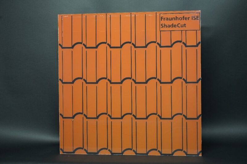 Auf dem Foto ist eine Folie zu sehen, die auf einer etwa quadratischen Fläche rote Dachziegel imitiert, der Hintergrund ist dunkelgrau.