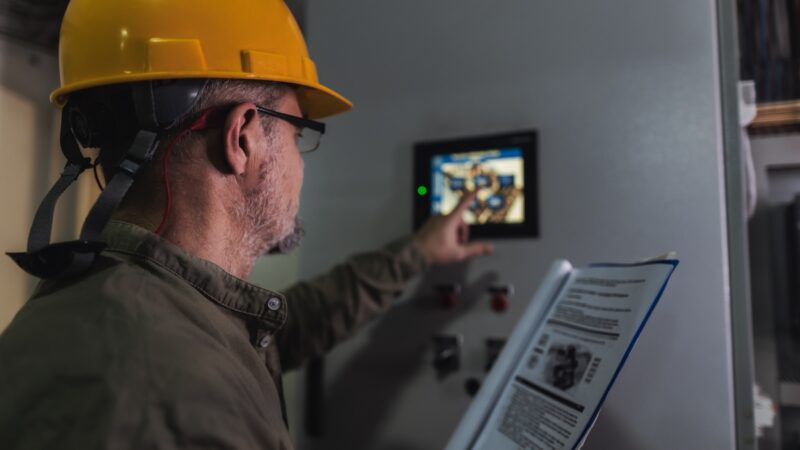 Mann mit gelbem Helm drückt auf Display an Heizungsanlage - Symbolbild für Bio-Heizöl von Shell.