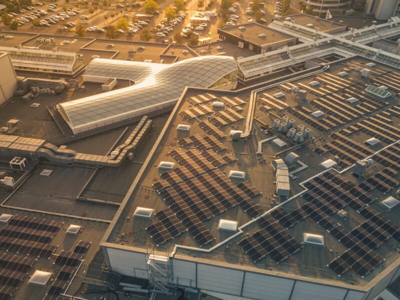 Luftbild zeigt Photovoltaik-Anlage auf Dach des Shoppingcenters bei schräg stehender Sonne.