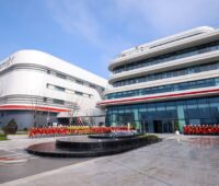 Blumen geschmückte Eingangsfront des neuen Fabrikgebäudes von Sigenergy in China zur Produktion von Speicher- und Wechselrichtern.