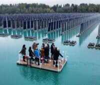 Personen auf schwimmender Plattform betrachten schwimmende Anlage mit vertikal aufgestellten PV-Modulen.