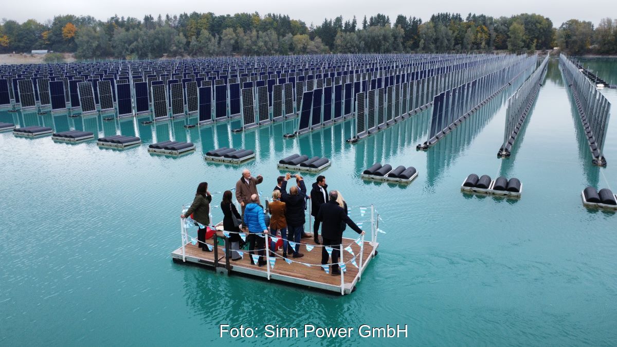 Personen auf schwimmender Plattform betrachten schwimmende Anlage mit vertikal aufgestellten PV-Modulen.