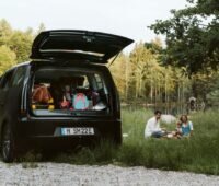 Ein Solaruto mit geöffneter Ladefläche und einer Kleinfamilie auf grüner Wiese.