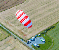 Ein rot-weiß gestreifter Kiteschirm über Ackerflächen zeigt die Flexibilität der Flugwindenergie.