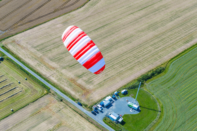 Ein rot-weiß gestreifter Kiteschirm über Ackerflächen zeigt die Flexibilität der Flugwindenergie.