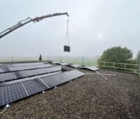 Ein Kran hebt faltbare PV-Module auf ein Flachdach.