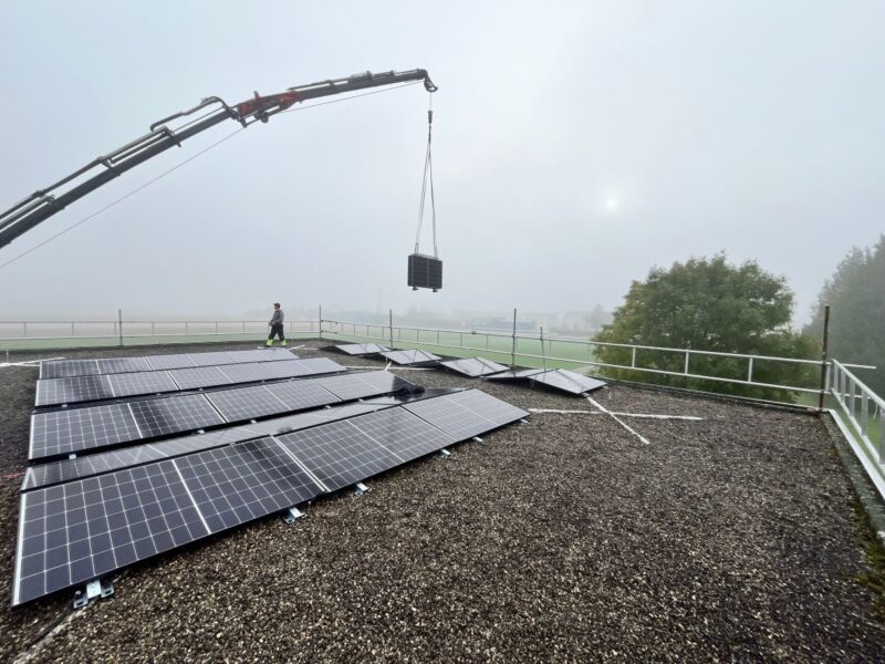 Ein Kran hebt faltbare PV-Module auf ein Flachdach.