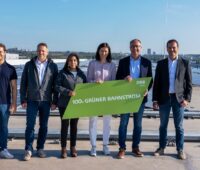 Menschen vor Solar-Anlage mit Schild, auf dem "grüner Bahnstrom" steht