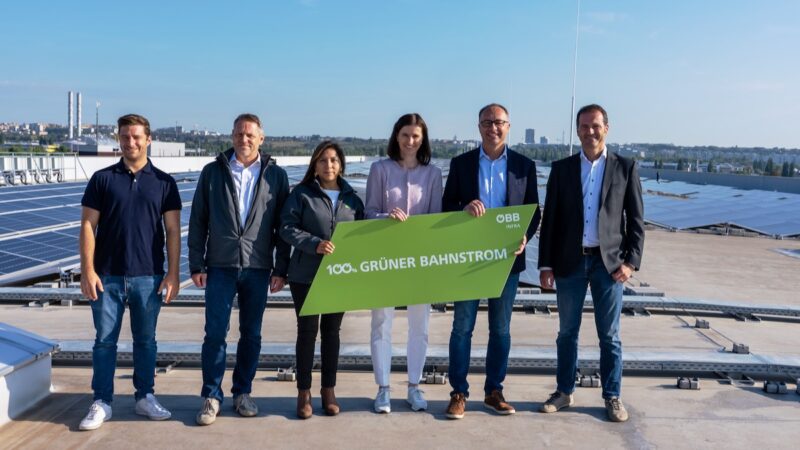 Menschen vor Solar-Anlage mit Schild, auf dem "grüner Bahnstrom" steht