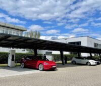 Solar-Carport auf Firmenparkplatz, darunter einige geparkte Autos und Ladesäulen.