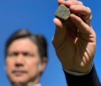 Ein Mann hält ein graues Stück Stein vor blauem Himmel - erster Solarklinker für die Zement-Herstellung mit Solarer Prozesswärme