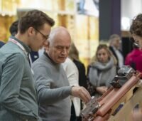 Menschen stehen vor Dachziegel mit Solar-Montage-Set an einem Messestand - Solar Solutions in Düsseldorf