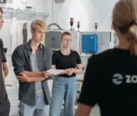 Mehrere junge Menschen stehen im Kreis in einem Raum mit technischen Geräten - Schulung für Photovoltaik-Hilfskräfte.