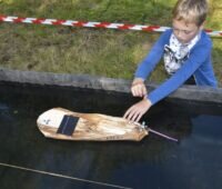 Ein Junge mit einem selbst gebauten Solarboot aus Bananenblättern.