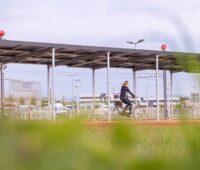 Foto zeigt Blick über eine Wiese auf den Solardach-Radweg und eine Radlerin.