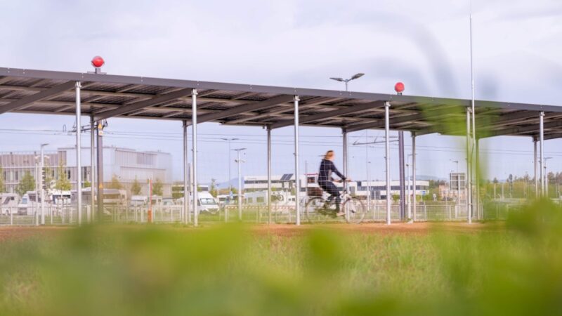 Foto zeigt Blick über eine Wiese auf den Solardach-Radweg und eine Radlerin.
