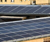 Zwei leicht geneigte mit Photovoltaik belegte Dächer von älteren Gewerbehallen.