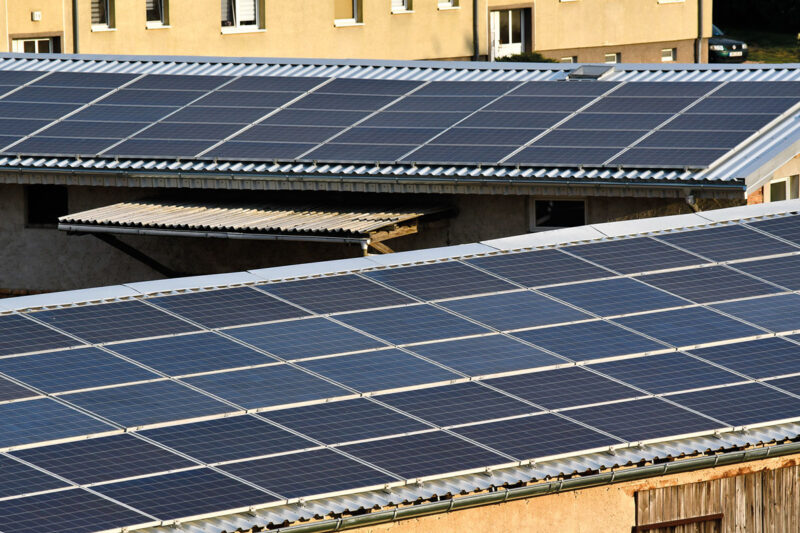 Zwei leicht geneigte mit Photovoltaik belegte Dächer von älteren Gewerbehallen.