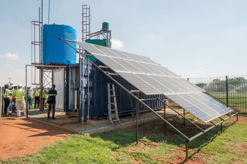 Ein Solarpanel vor einem Wellblechcontainer mit Wassertank auf dem Dach.