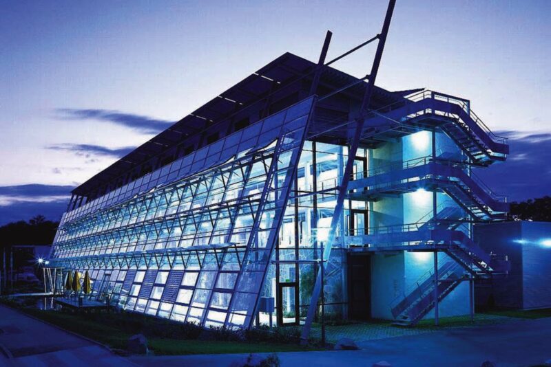 Eine bei Nacht im blauen Licht leuchtende Fassade eines Industriegebäudes: der ersten Solar-Fabrik in Freiburg.