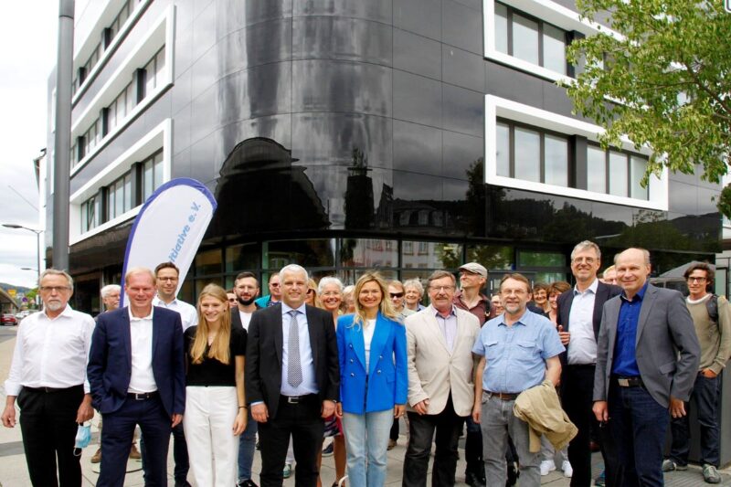 2 Dutzend Personen vor einem Gebäude mit schwarzer Fassade.