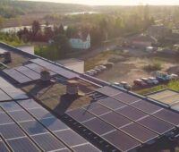 Blick auf ein Flachdach m,it Solarmodulen bei tioefstehender Sonne am Rande eines Wäldchens.