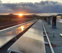 Blick über ein Dach mit Solarmodulen im Abendlicht.