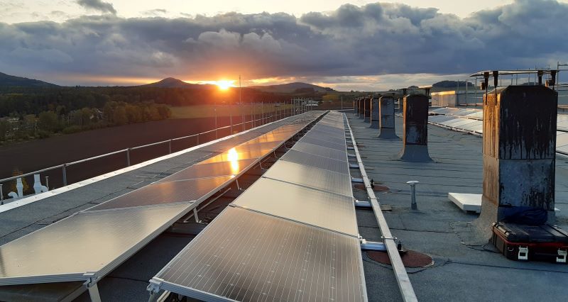 Blick über ein Dach mit Solarmodulen im Abendlicht.