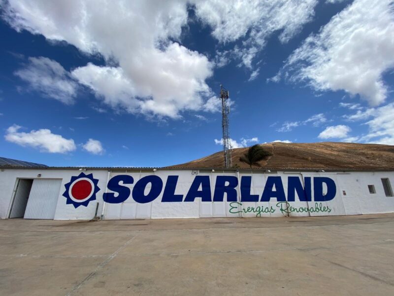 Schriftzug Solarland auf einer Mauer mit Sonne sowie einer Windkraftanlage im Hintergrund.