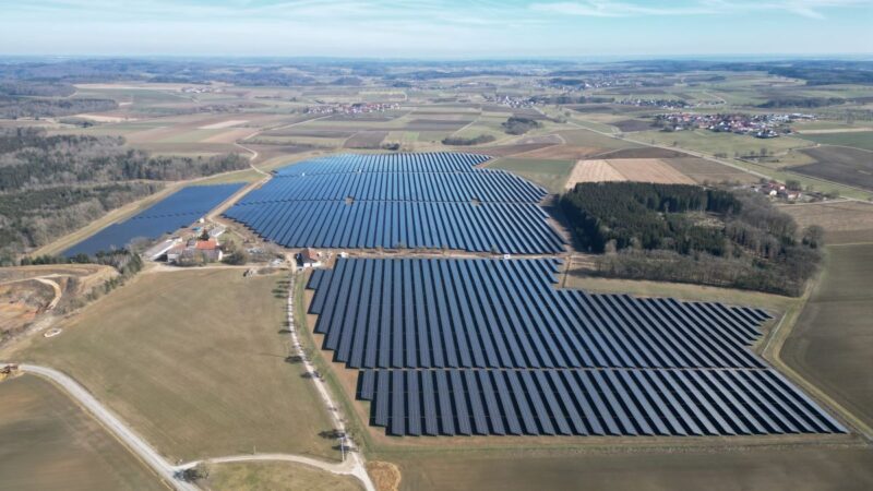 Luftbild eines Freiflächen-Solarparks auf eher braunen Wiesen.