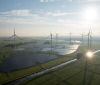 Luftbild zeigt großen PV-Park unter Windenergieanlagen im grünen Flachland.