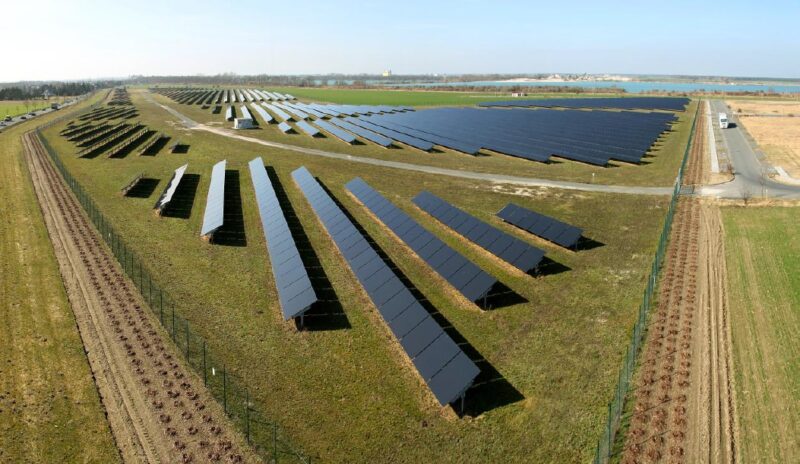Ein Freiflächensolarpark im Flachland am Rande eines kleinen Binnengewässers.