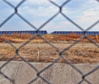 Hinter einem Zaungeflecht ist ein Solarpark in trockener Erde zu sehen. Standort ist das mittelamerikanische Honduras.