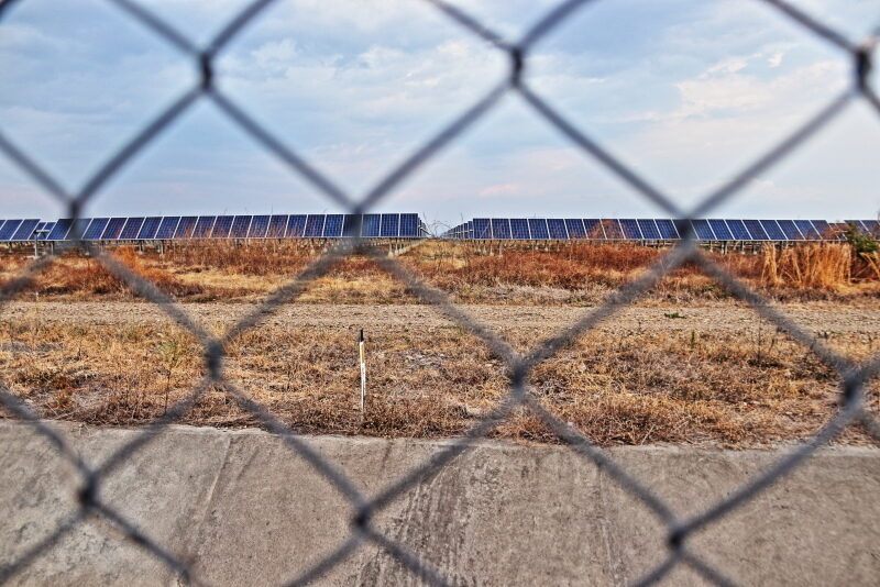 Hinter einem Zaungeflecht ist ein Solarpark in trockener Erde zu sehen. Standort ist das mittelamerikanische Honduras.