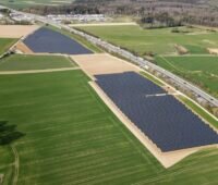 Luftbild eines Solarparks an der Landstrasse neben landwirtscatlichen Grünflächen.