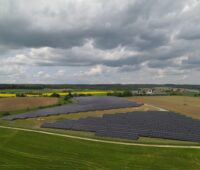 Luftbild eines Freiflächensolarkraftwerks im Flachland, umgeben von Wiesen.