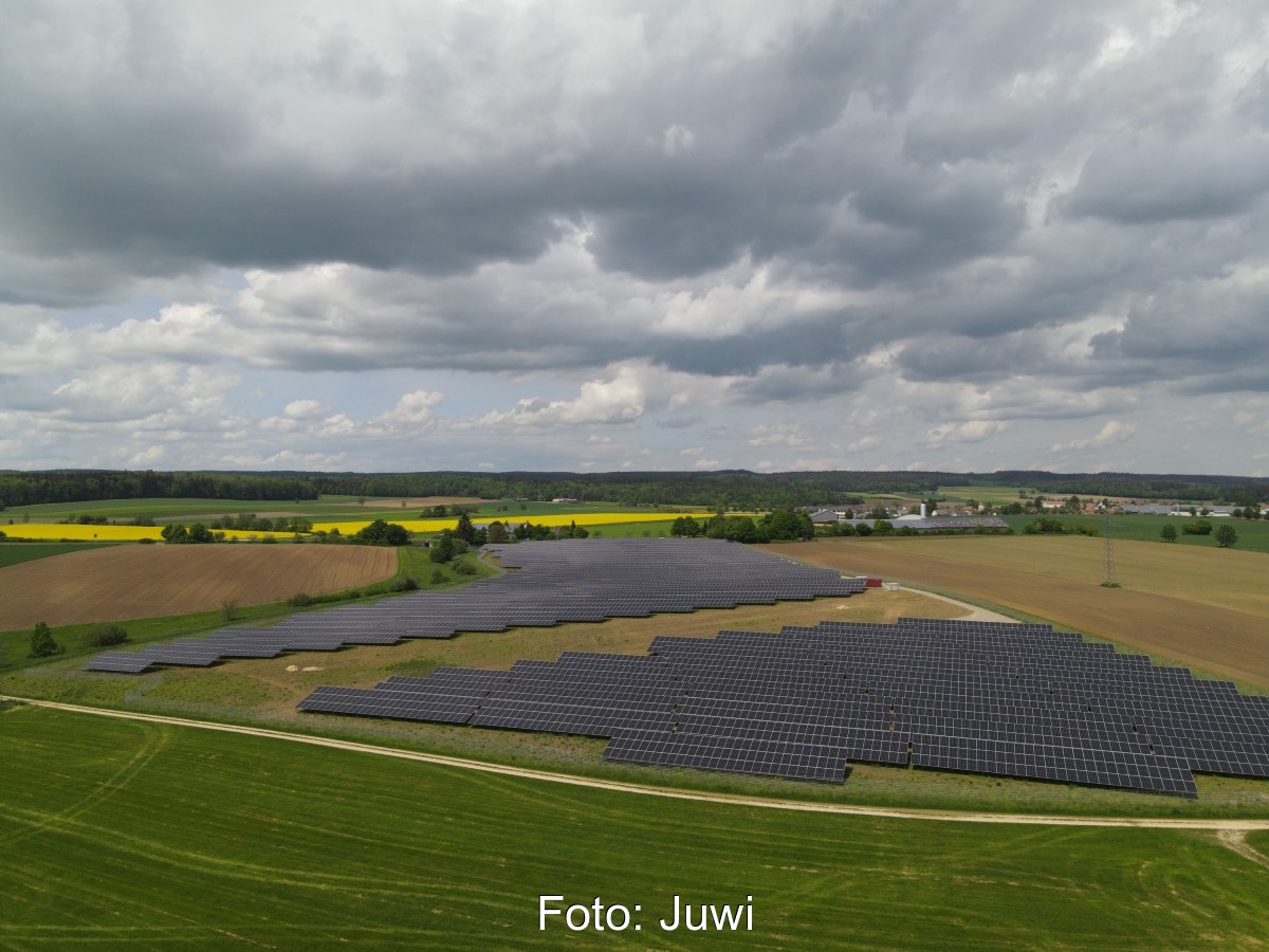 Luftbild eines Freiflächensolarkraftwerks im Flachland, umgeben von Wiesen.