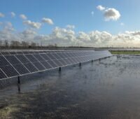 Im Vordergrund eine Wasserfläche in einem wiedervernässten Moor. Links im Bild eine Reihe aufgeständerter Photovoltaik-Module.