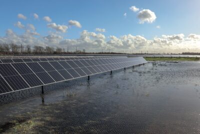 Im Vordergrund eine Wasserfläche in einem wiedervernässten Moor. Links im Bild eine Reihe aufgeständerter Photovoltaik-Module.