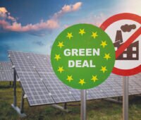 Symbolbild für EU-Solarstrategie und ETS-Reform: Schilder Green Deal und Abgase verboten vor einer Freiflächen-Solaranlage