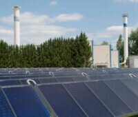 Solarthermieanlage in Vordergrund, Fernwärme-Heizkraftwerk Bernburg im Hintergrund - Symbolbild für BEW-Förderung