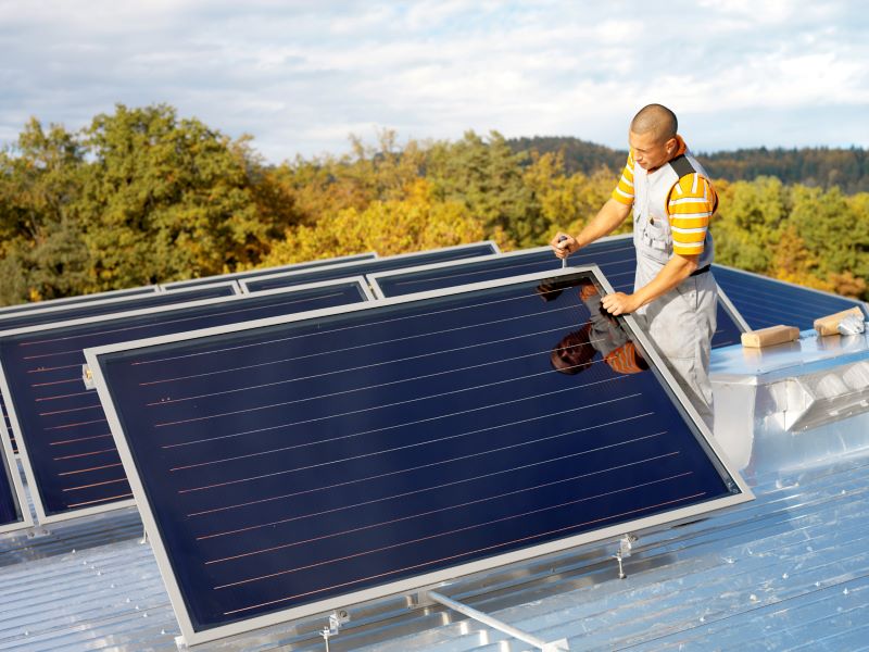 Ein Monteur installiert auf einem Flachdach Solarthermie-Kollektoren.