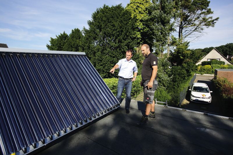 Zwei Personen im Gespräch auf einem Dach und betrachten dabei einen solarthermischen Kollektor